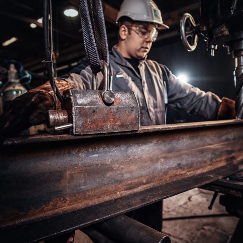 Man in helmet is moving a piece of rail at metal factory.